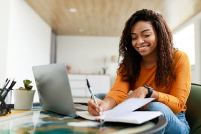 Smiling young black woman sitting at desk working on laptop